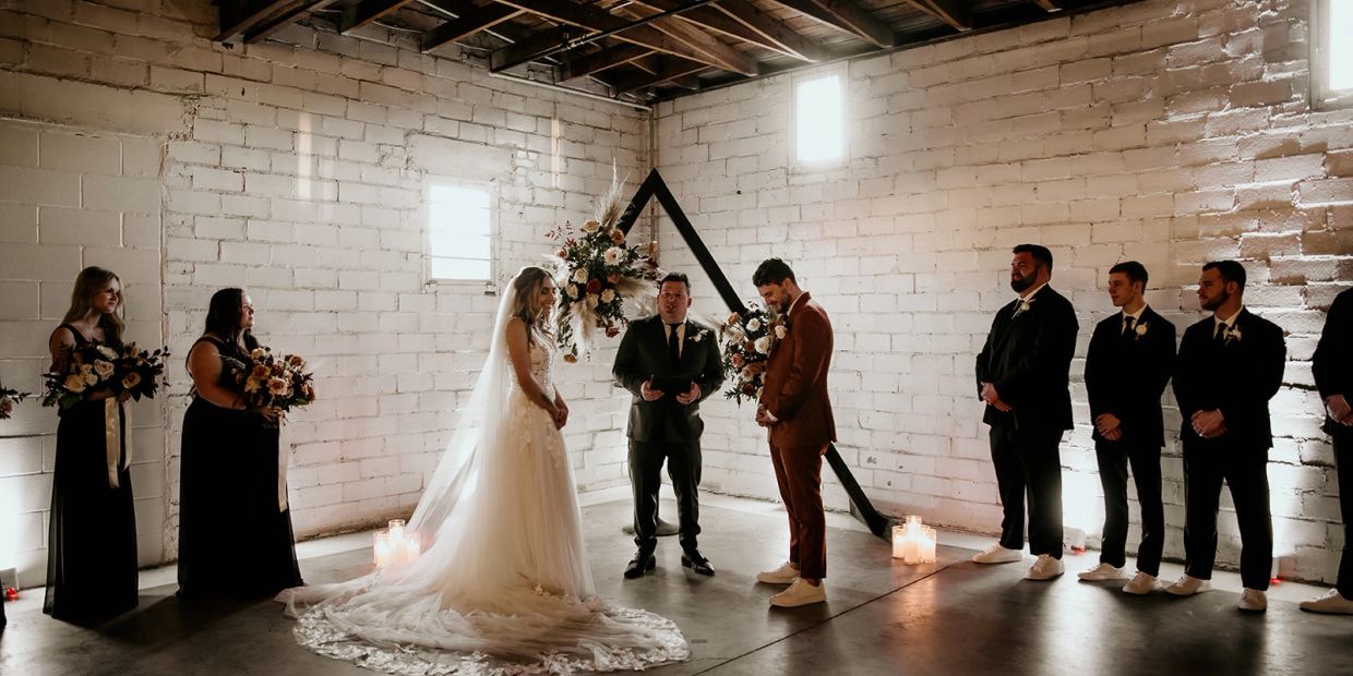 Bride and groom stand with wedding party in industrial-style venue.