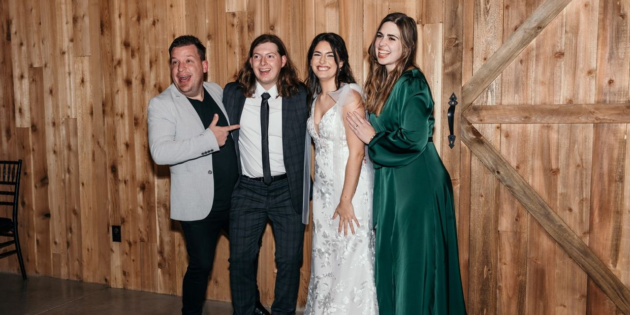 DFW wedding officiant celebrating with the newlyweds and a guest at a rustic wood-paneled reception venue