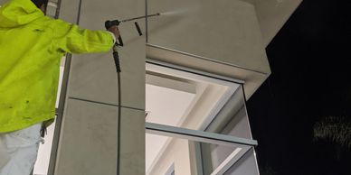 Person in yellow jacket pressure washing a building's exterior at night.