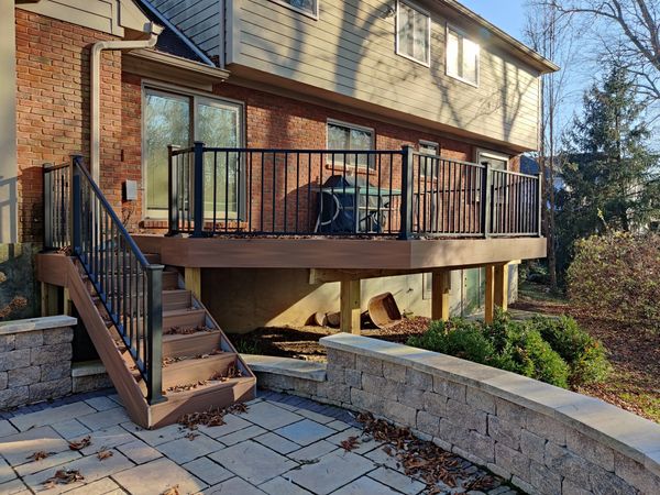 A raised wooden deck with black railings and stairs leading to a stone patio.