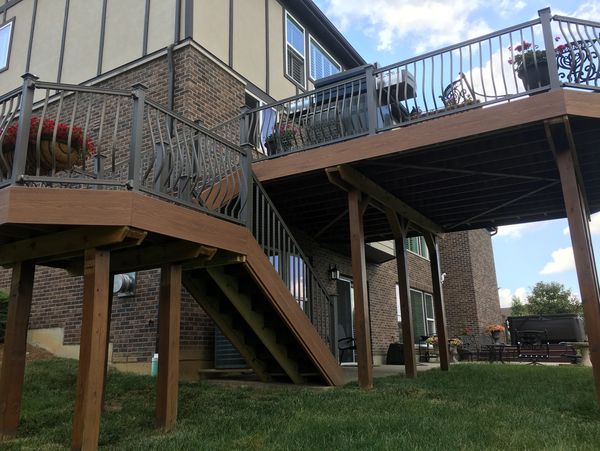 Elevated wooden deck with metal railings and stairs attached to a brick house.