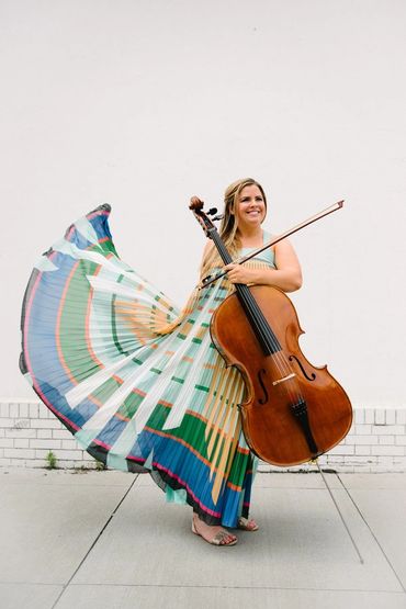Woman joyfully playing cello in colorful flowing dress.