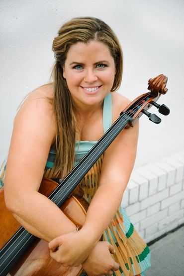 Smiling woman holding a cello against a white wall.