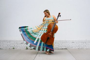 Woman in a colorful dress playing the cello outdoors.