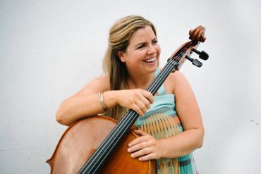 A smiling woman playing a cello against a plain white background.