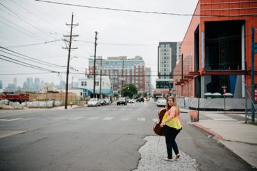 Woman crossing an urban street carrying a guitar case.
