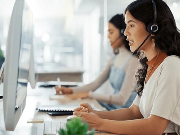 Customer service agents working with headsets at computers in an office.
