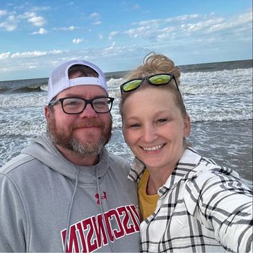 Smiling couple taking a selfie at the beach with waves in the background.