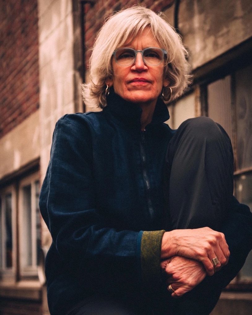 Woman with glasses and white hair sitting thoughtfully outdoors.