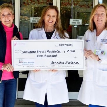 Three women holding a large donation check outside a building.
