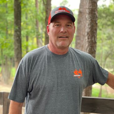 A man wearing a gray shirt and cap standing outdoors.