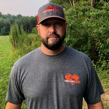Man standing outdoors wearing a Sportsman's Grill shirt and hat.