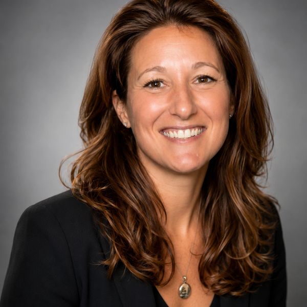 Professional woman with long brown hair smiling in a black blazer.