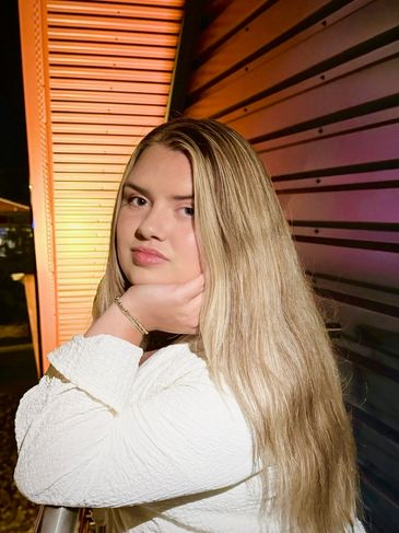 Young woman with long blonde hair posing by a textured wall.
