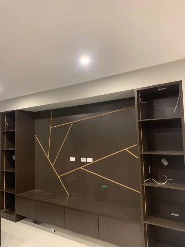 Modern dark wood entertainment unit with geometric gold accents under ceiling light.