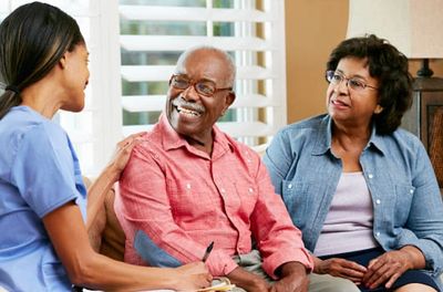 A nurse talking with an elderly couple in their home.