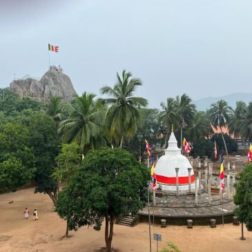 White stupa with flags and rocky hill in the background.