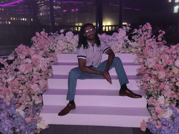 Man sitting on pink steps surrounded by purple and white flowers at night.