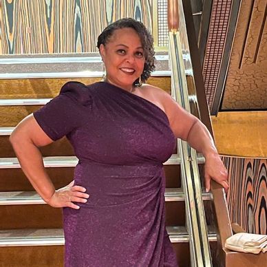 A woman in a purple one-shoulder dress posing confidently on stairs.