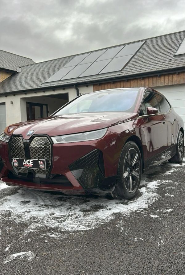 Maroon BMW parked in front of a house with solar panels.