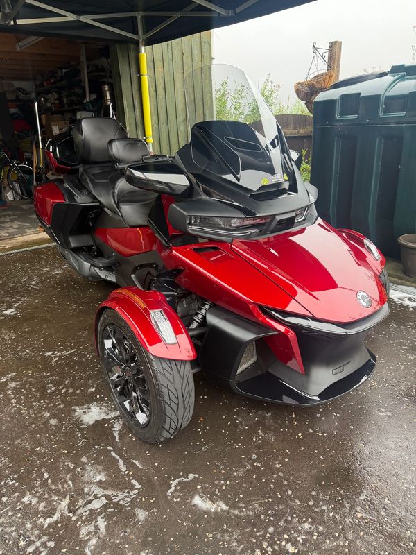 Red three-wheeled motorcycle parked near a garage.