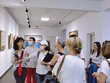 Group of people observing artwork in a gallery, some wearing masks.