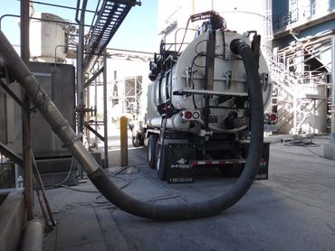 A large industrial vacuum truck with a thick hose attached in a factory setting.