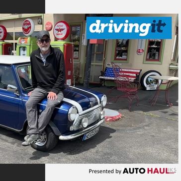 Man sitting on a blue vintage Mini Cooper outside a retro gas station.