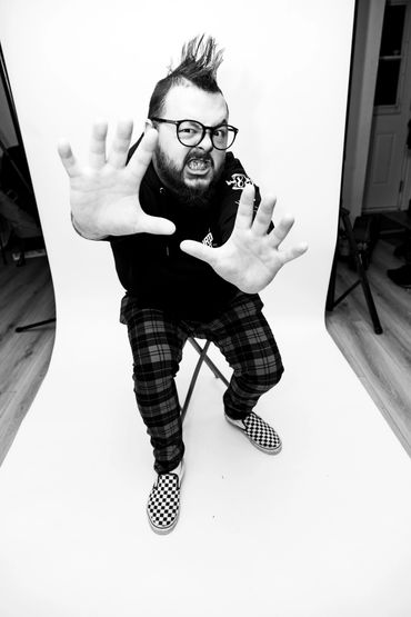 

Man with mohawk and glasses making expressive hand gestures in black and white photo.