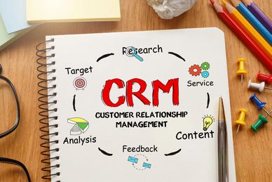 notebook on a table with writing on it regarding CRM and what it is and with pencils and thumb tacksh