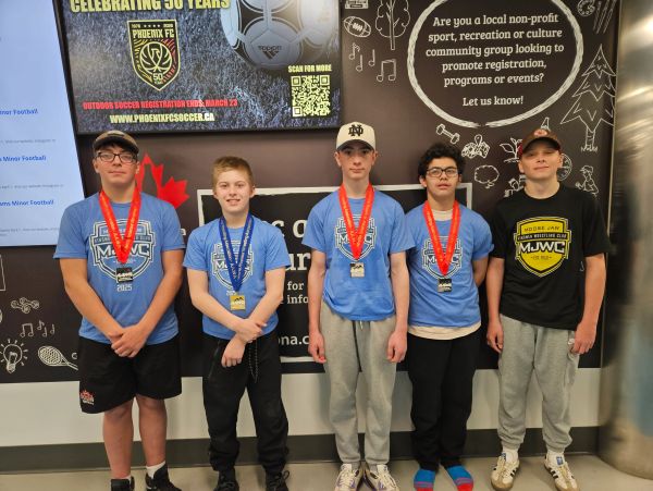 Five boys wearing medals and sports t-shirts posing indoors.