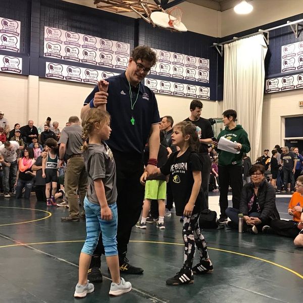 A coach talks to two young wrestlers in a crowded gym during a wrestling event.