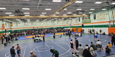 A busy gym with wrestling mats and spectators for a wrestling event.