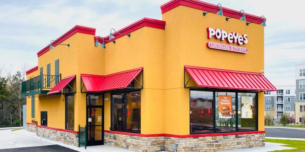 Bright yellow and red Popeyes restaurant building on a clear day.