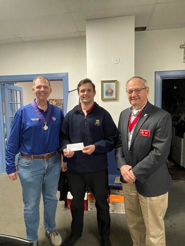 Three men posing indoors, one holding a check.