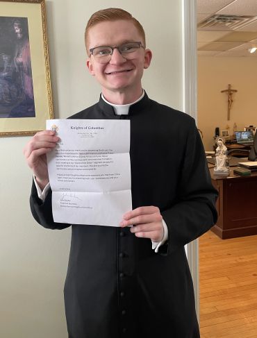 Young priest holding a letter with a smile.