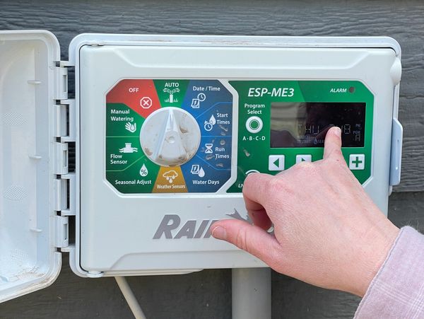 Hand adjusting settings on a Rain Bird ESP-ME3 irrigation controller.