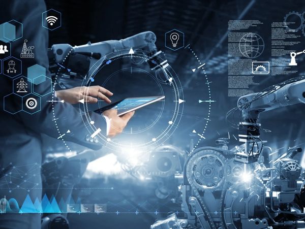 Engineer using a tablet to control robotic arms in a smart factory environment.