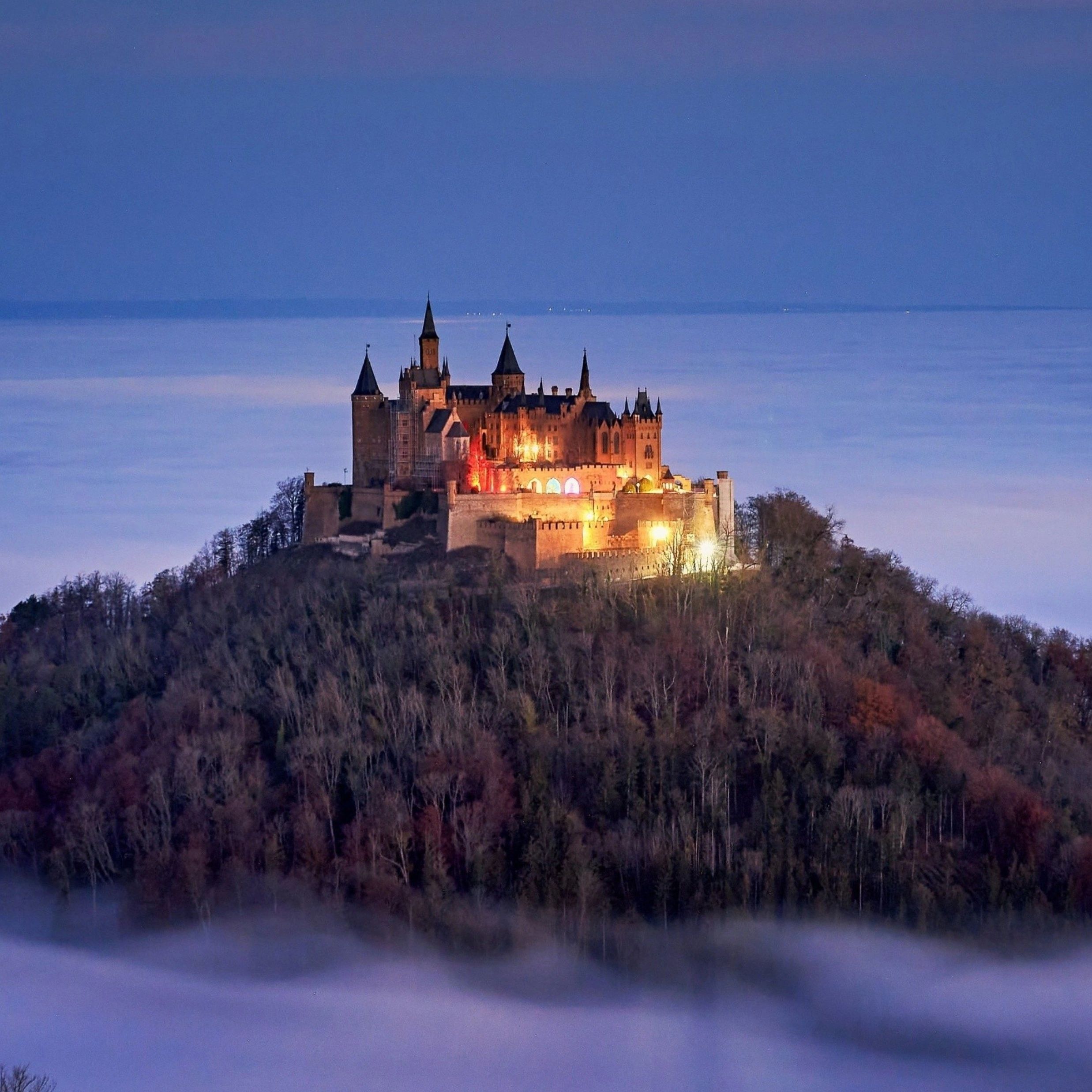 Castle illuminated on a hill surrounded by fog.