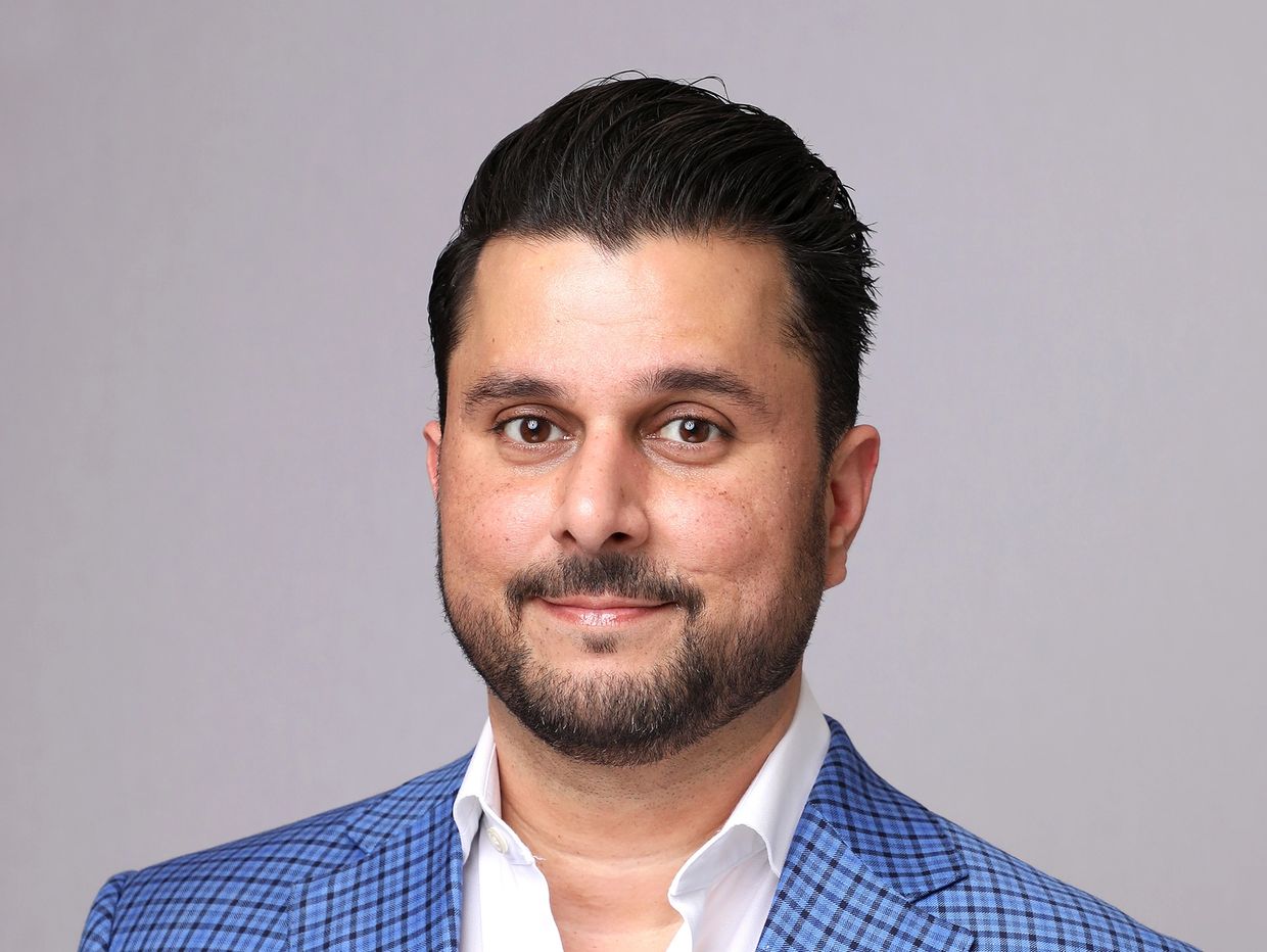 Man in a blue checkered blazer and white shirt posing for a portrait.