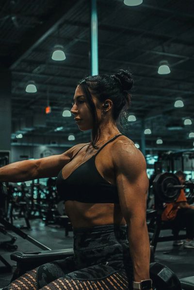 Woman lifting weights in a dimly lit gym, showing strong muscles.