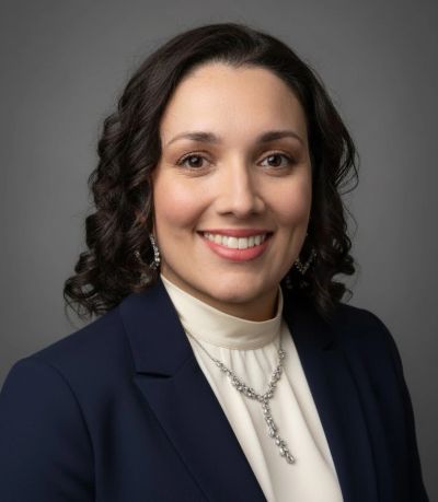 Professional portrait of a smiling woman with dark curly hair.