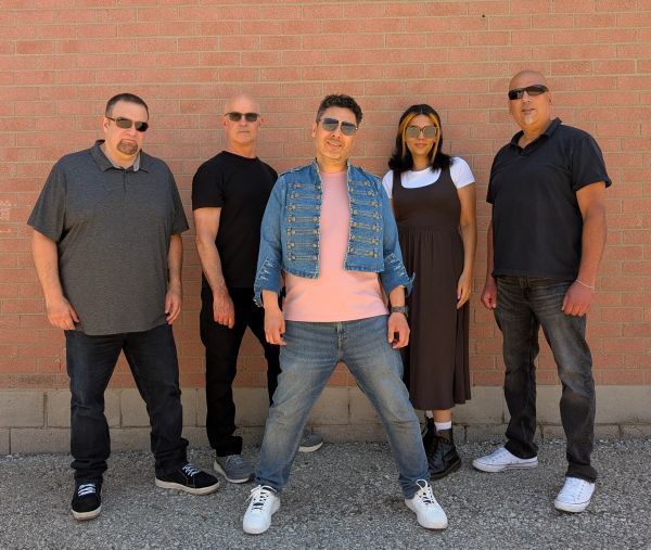 Group of five people posing against a brick wall.