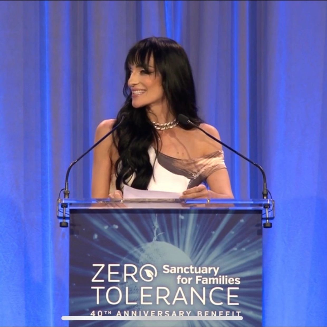 A woman smiles while speaking at a Zero Tolerance event podium.