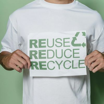 Person holding a sign promoting reuse, reduce, recycle in green text.