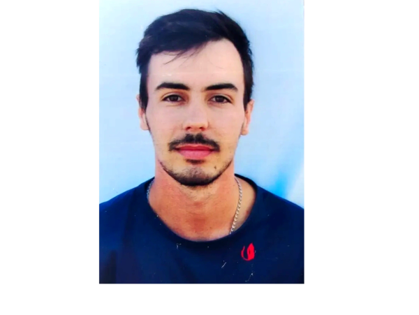 Portrait of a young man with dark hair and a chain necklace.