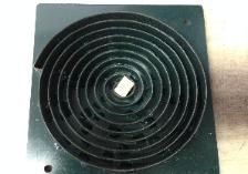 A square metal plate with a spiral-shaped groove and a small central square hole.