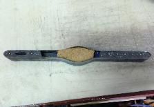 A worn-out leather strap with a padded center on a white surface.