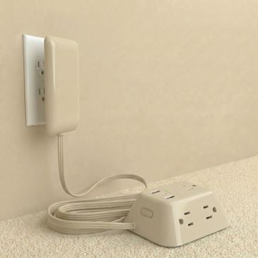 Beige power strip with coiled cord plugged into a wall outlet.