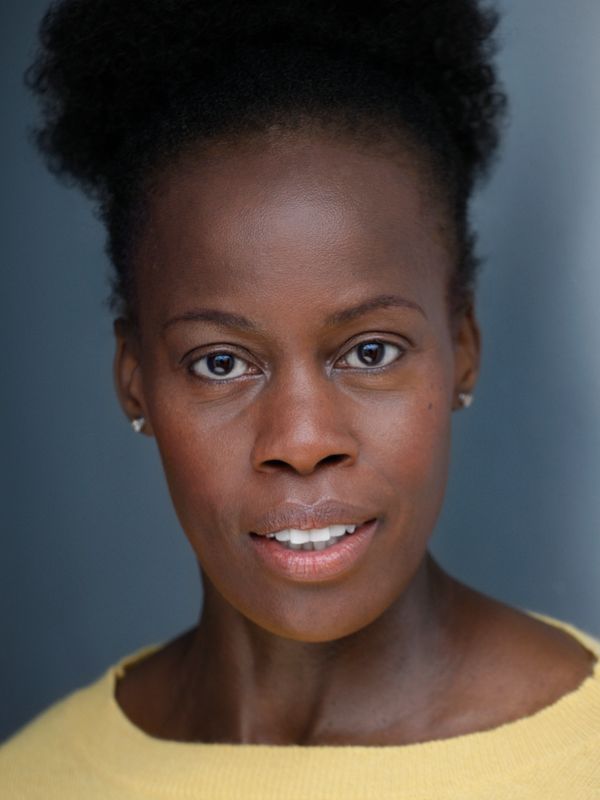 Close-up of a woman with natural hair and a yellow sweater against a blue background.
